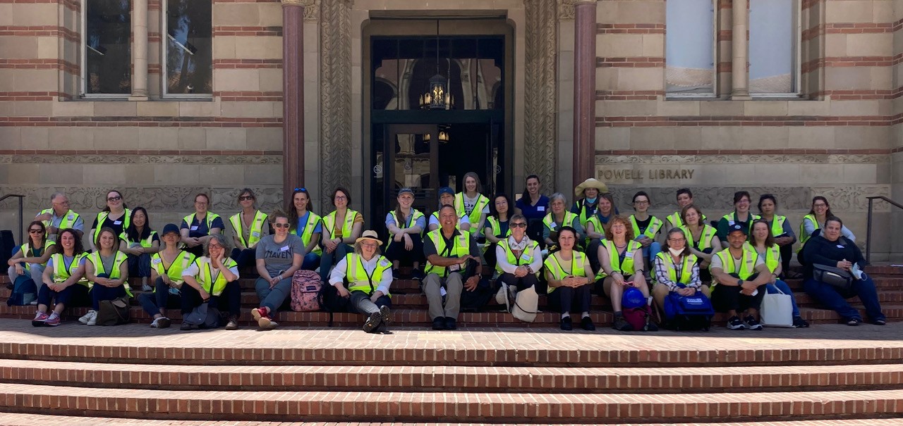 Group of individuals in yellow vests sitting on stairs in front of a building.