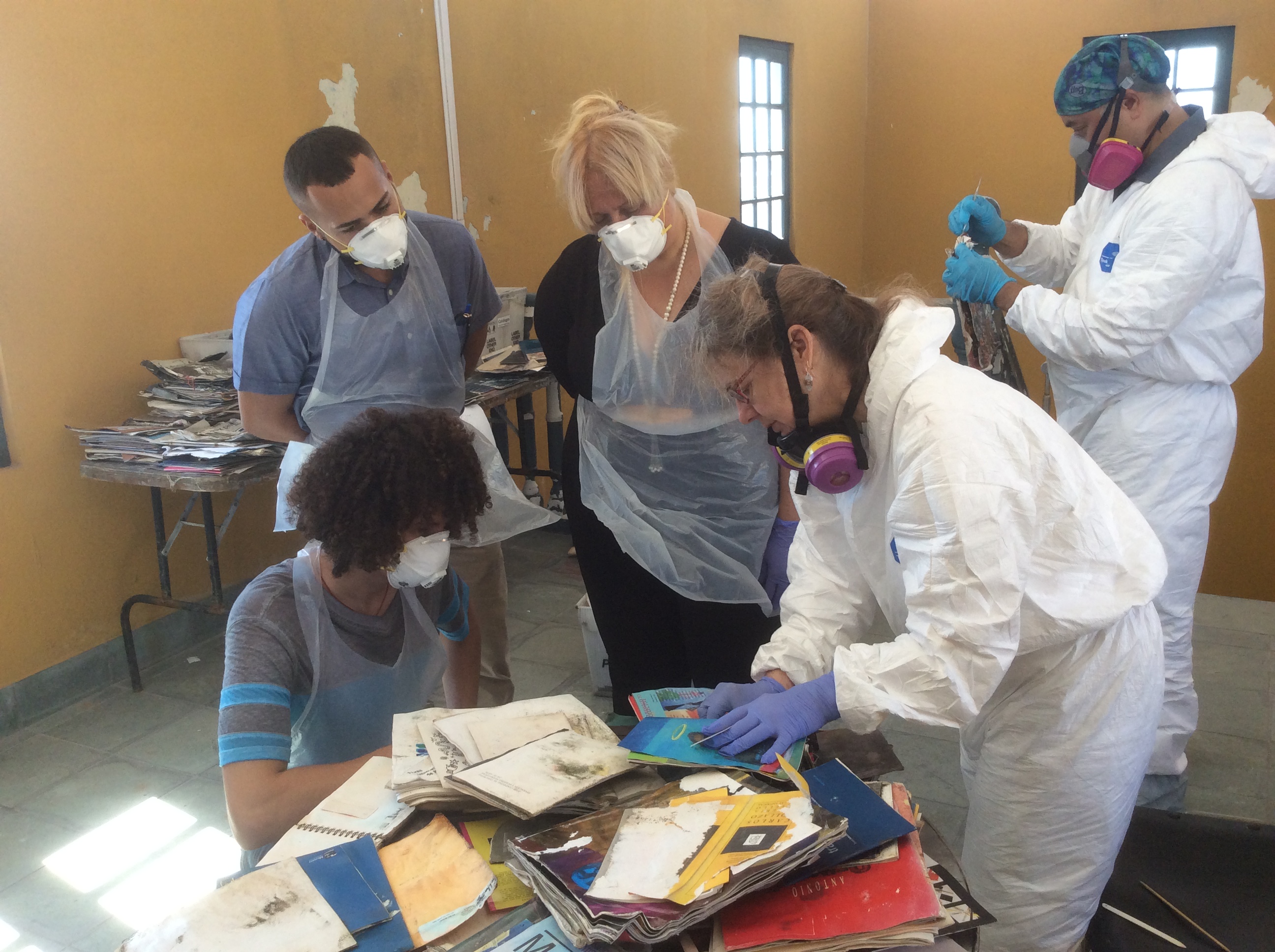 Five people wearing masks and PPE looking at damaged collections.