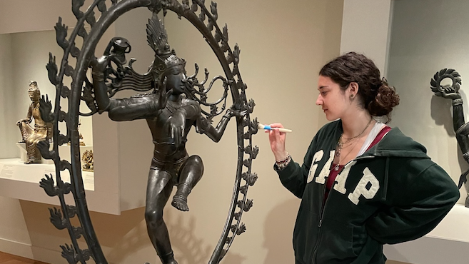 A woman dusting a metal sculpture in a gallery