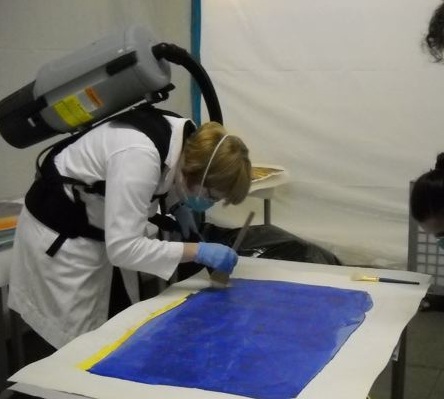 Woman in PPE cleaning a painting.