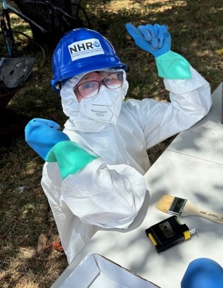 Woman in Tyvek suit, gloves, mask, and hard hat.