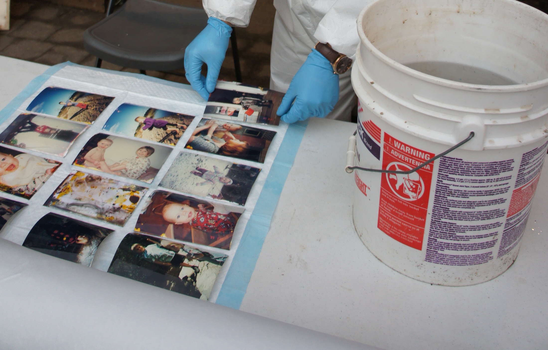 Photos laid out in a grid next to a bucket of water.