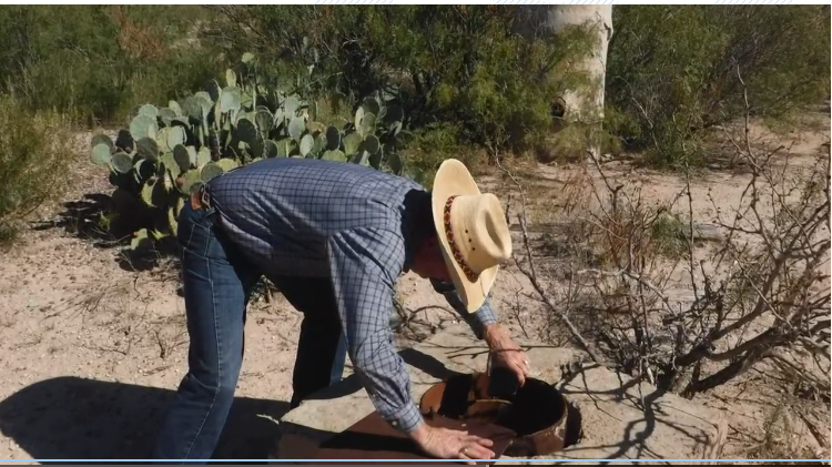 Man in cowboy hat leans over well