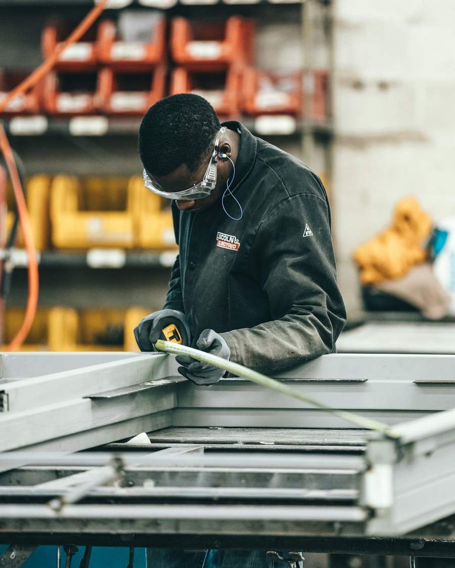 A manufacturing worker in safety glasses measuring a metal frame