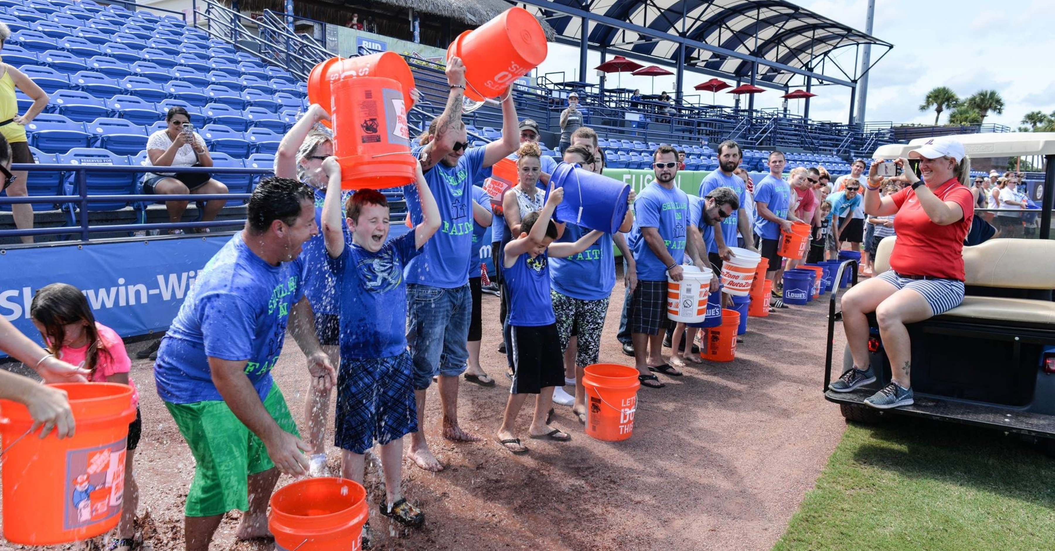 Families pouring ice buckets of water over their head in a line at a baseball field.