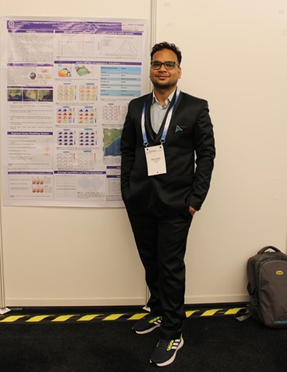 Smiling man wearing conference badge standing in front of a poster
