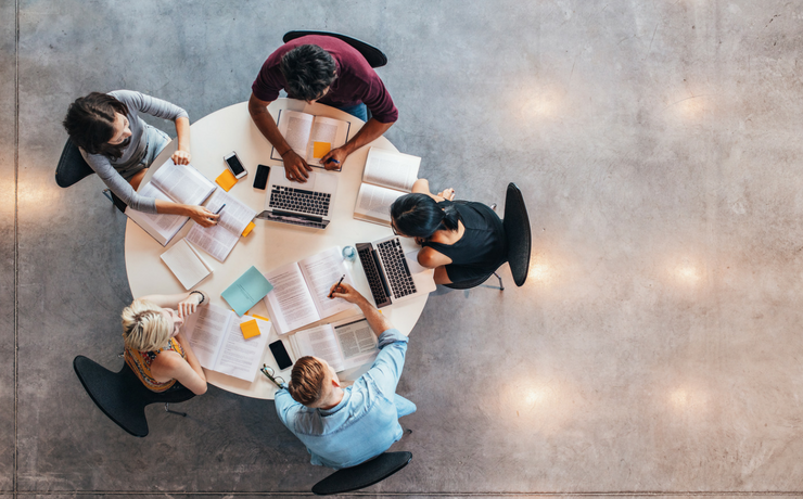 Overhead view of students sitting around a round table with books on the table studying together