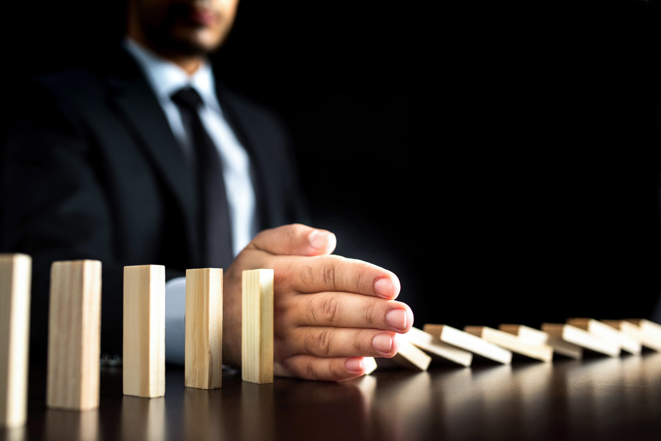 Businessman-Letting-Or-Preventing--Dominoes-Chain-Toppling-814347288_2122x1416.jpeg
