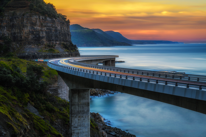 Sunset-over-the-Sea-cliff-bridge-along-Australian-Pacific-ocean-coast-with-lights-of-passing-cars-686552532_727x485.jpeg