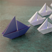 Image of a blue paper boat followed by white paper boats.