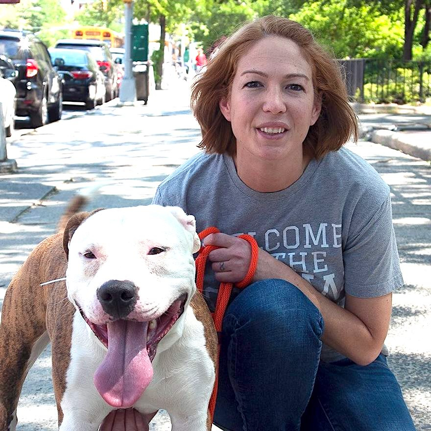 Kelly Duer crouching next to a happy dog on a city walkway