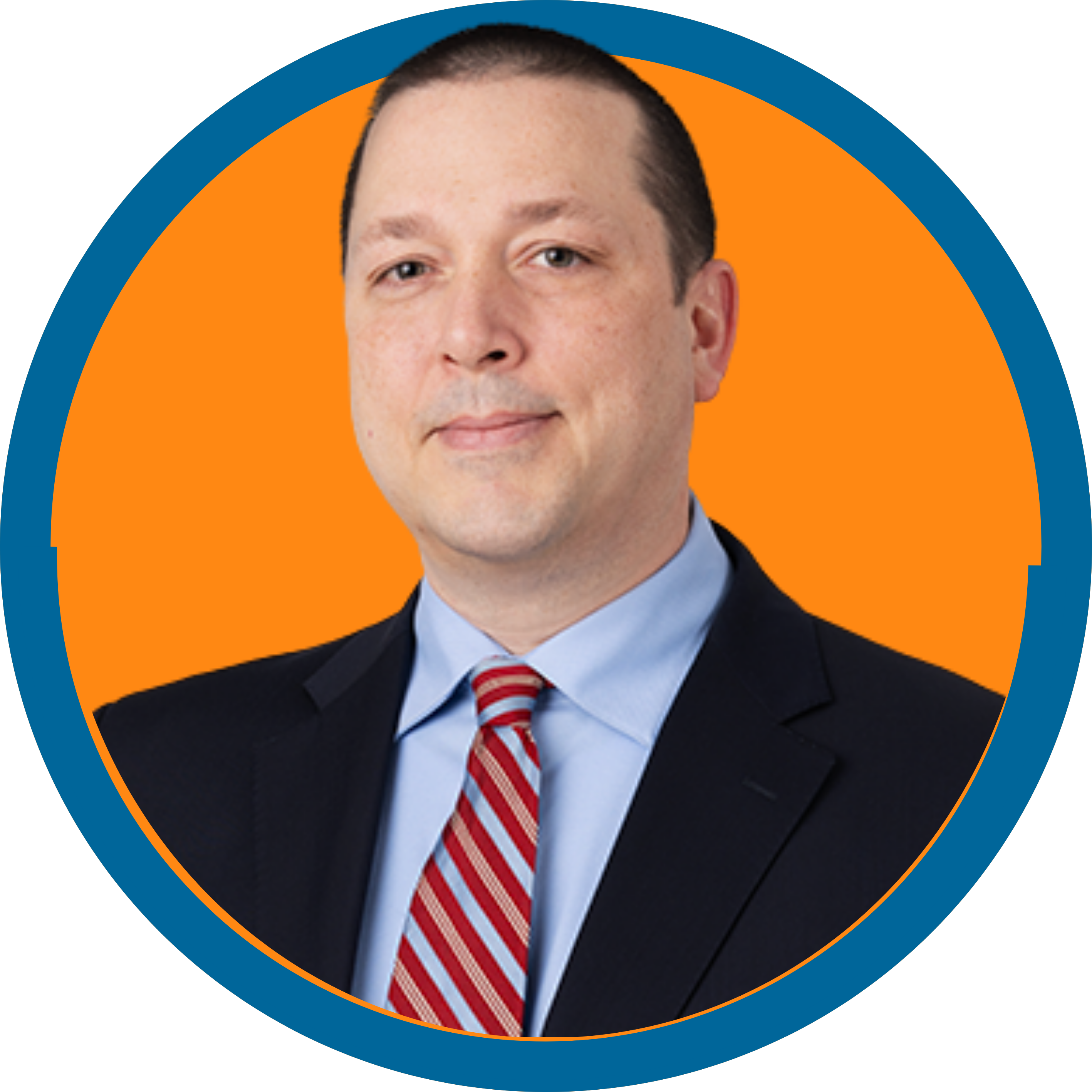 Image of a white man in a gray suit with short brown hair and a striped red and blue tie.