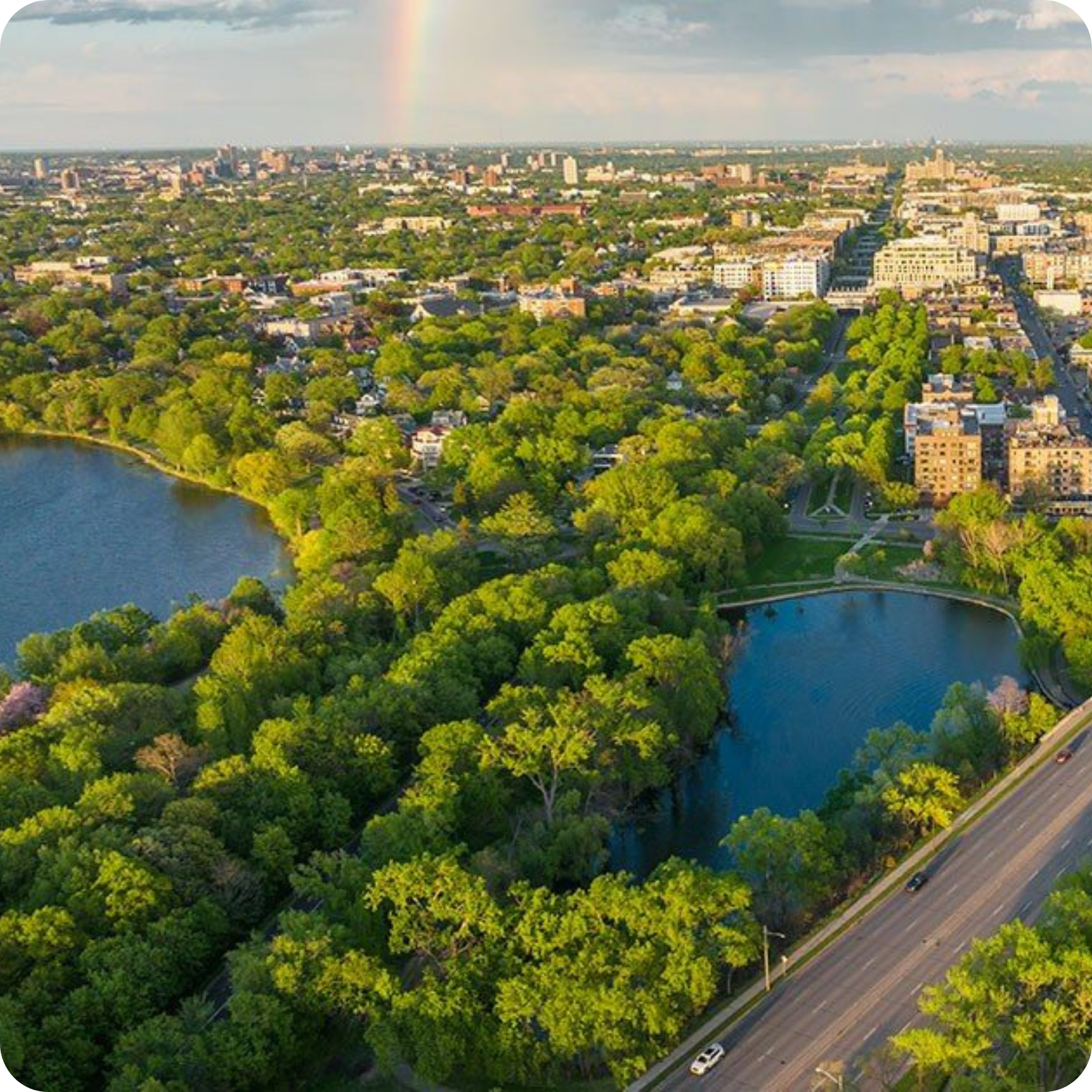 Drone image of a sprawling city with greenery, a rainbow, and two lakes in the foreground