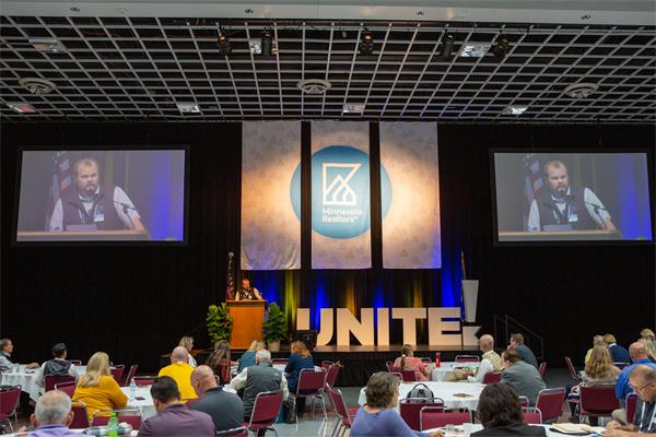 photo of a stage with a presenter speaking to a crowd