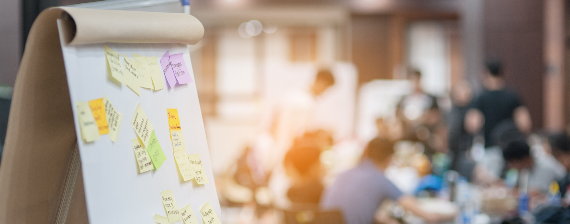 Image of a board with post it notes with teachers in the background