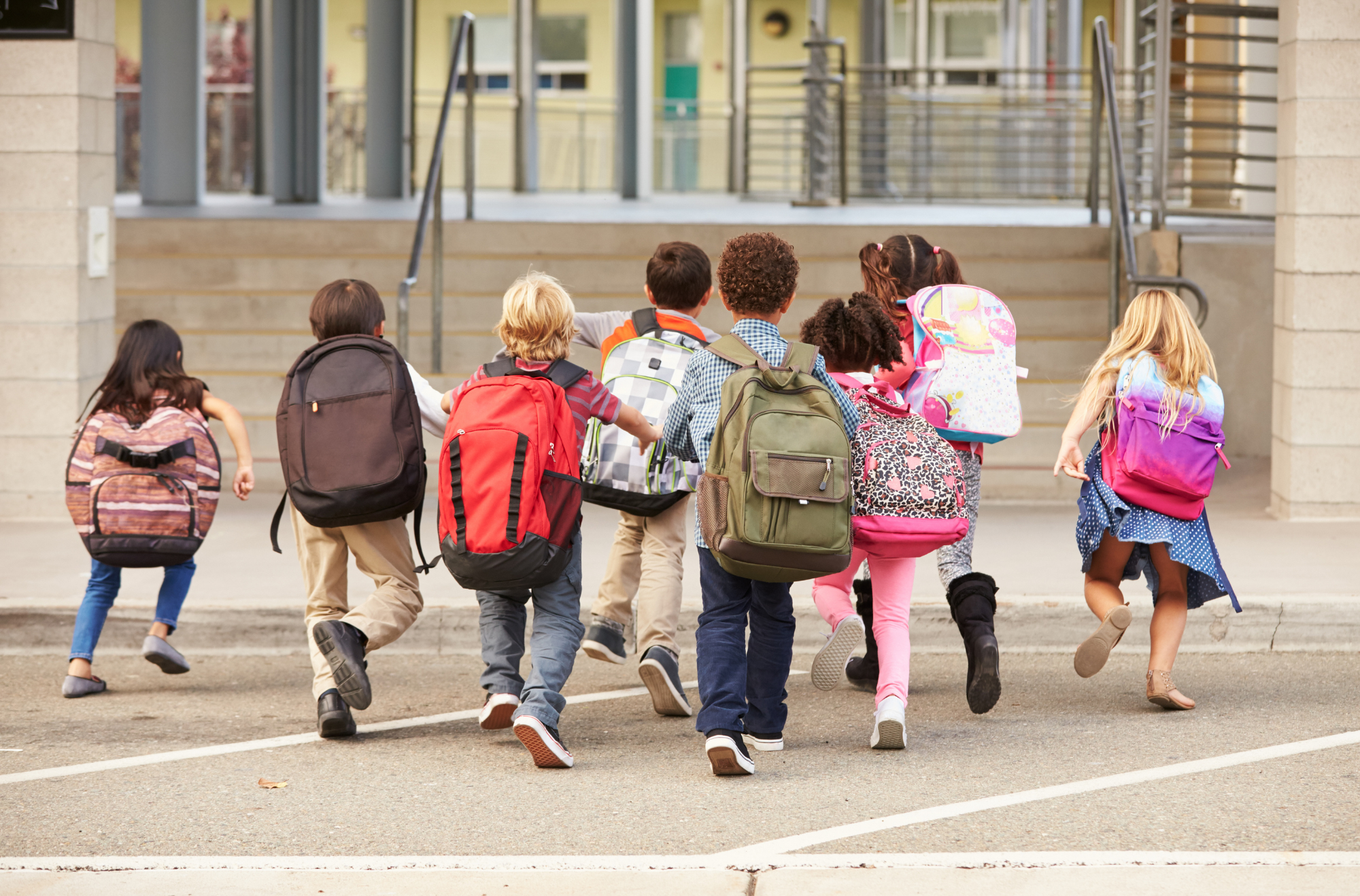 Elementary school children with backpacks running into school.