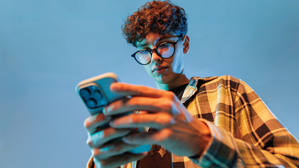 A student looks down at a cell phone in his hands