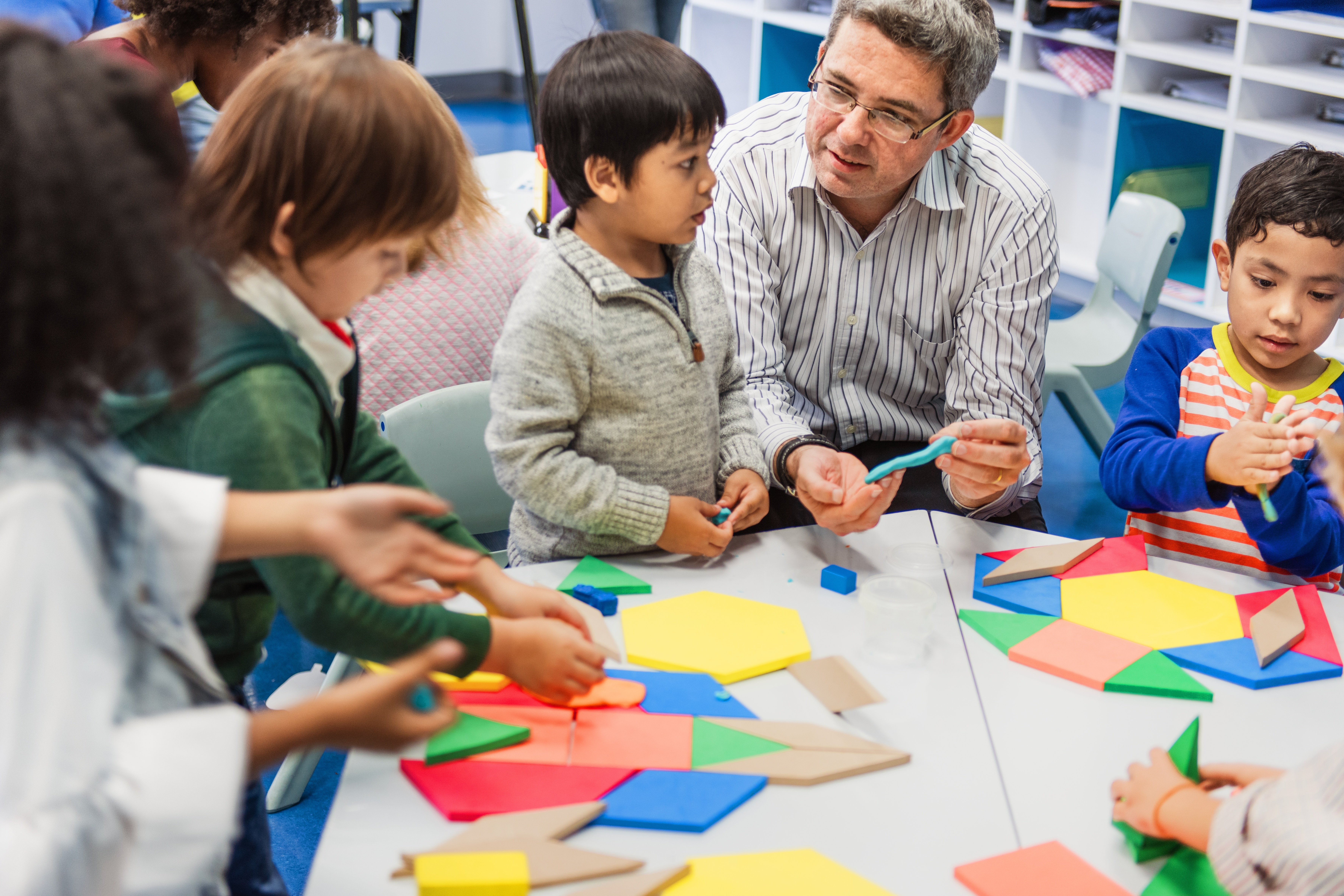 A teacher works with students at a table filled with geometric shapes