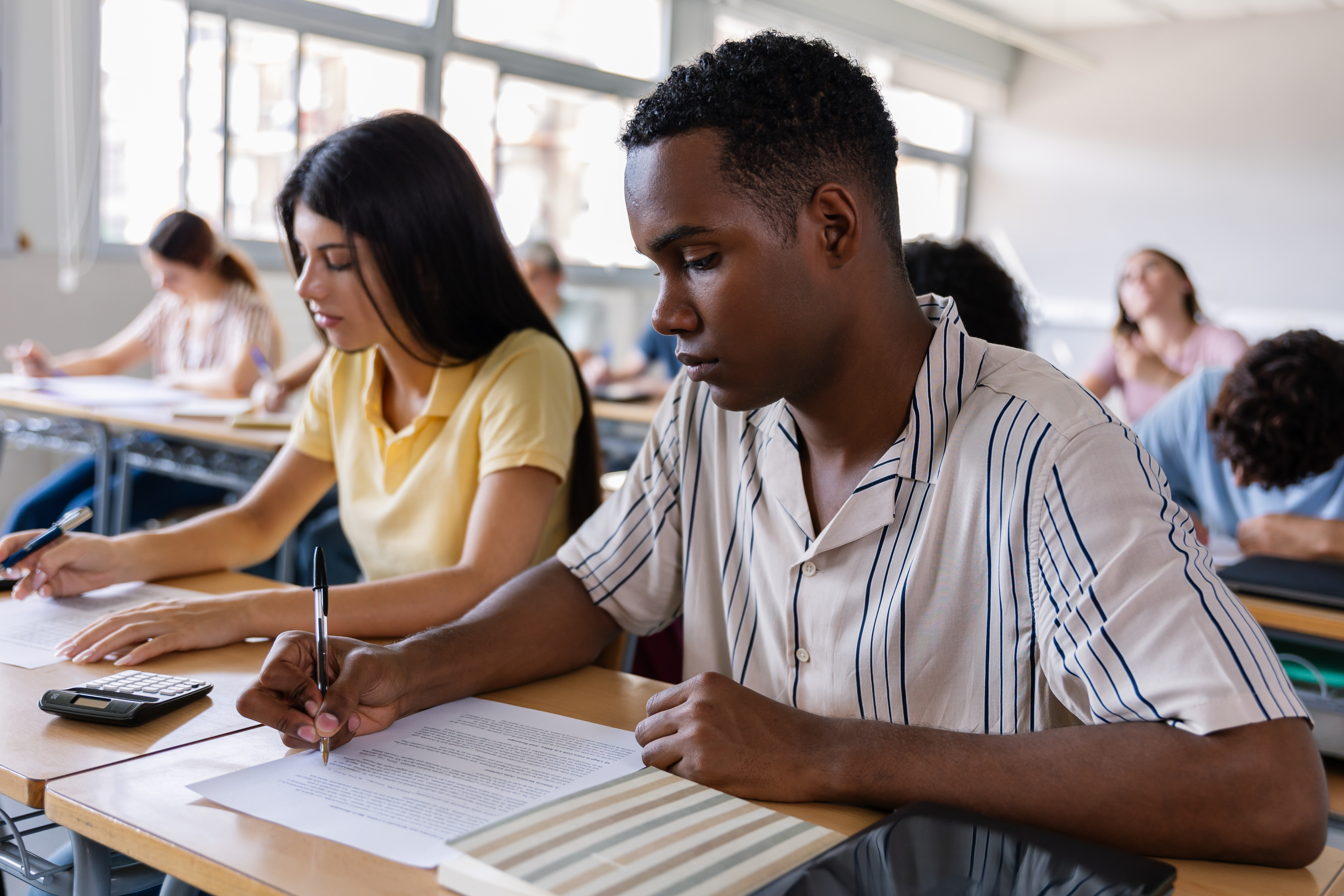 Students sitting in a row of classroom tables engaged in their schoolwork