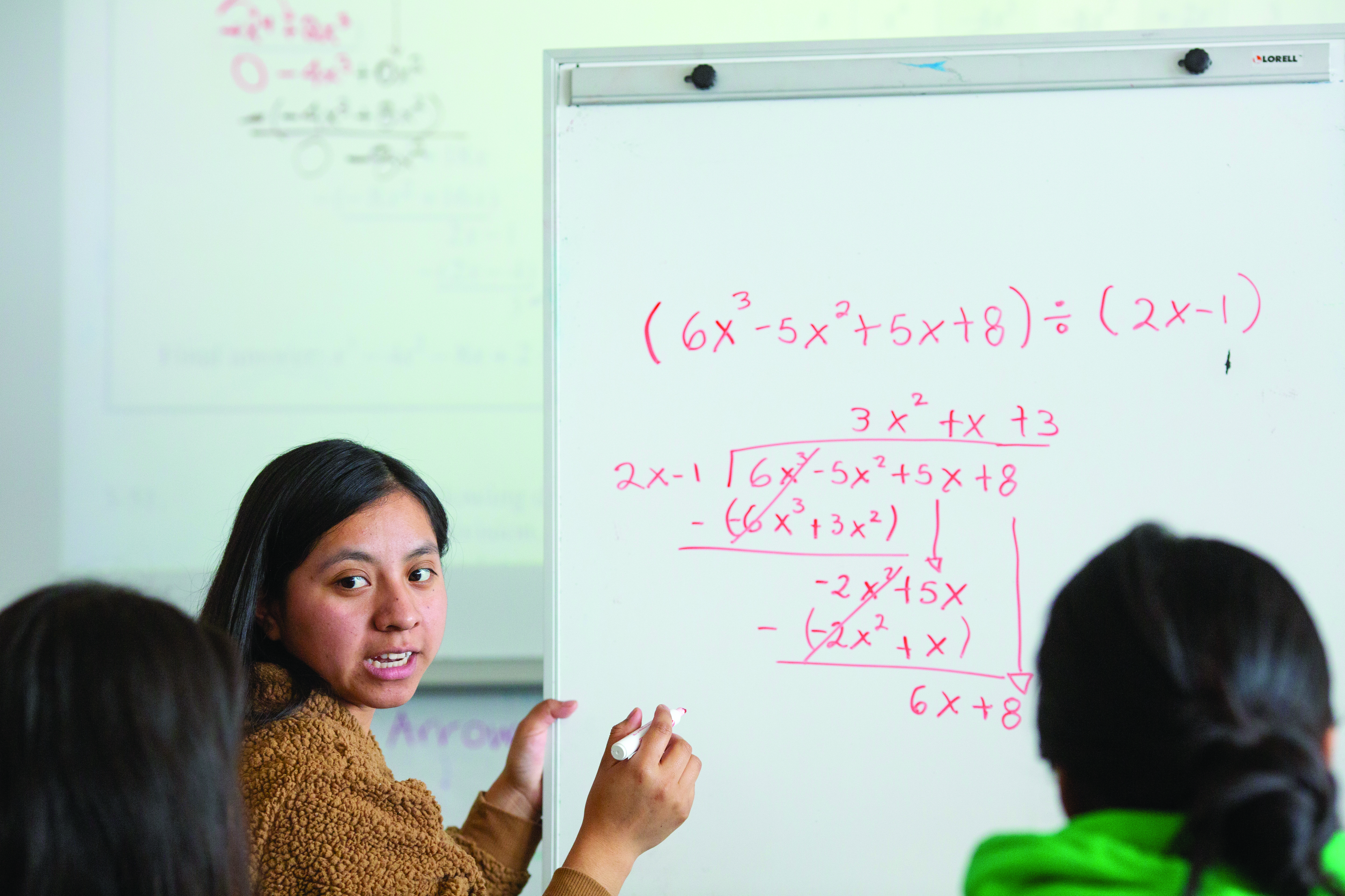 Students working on a math problem on a white board
