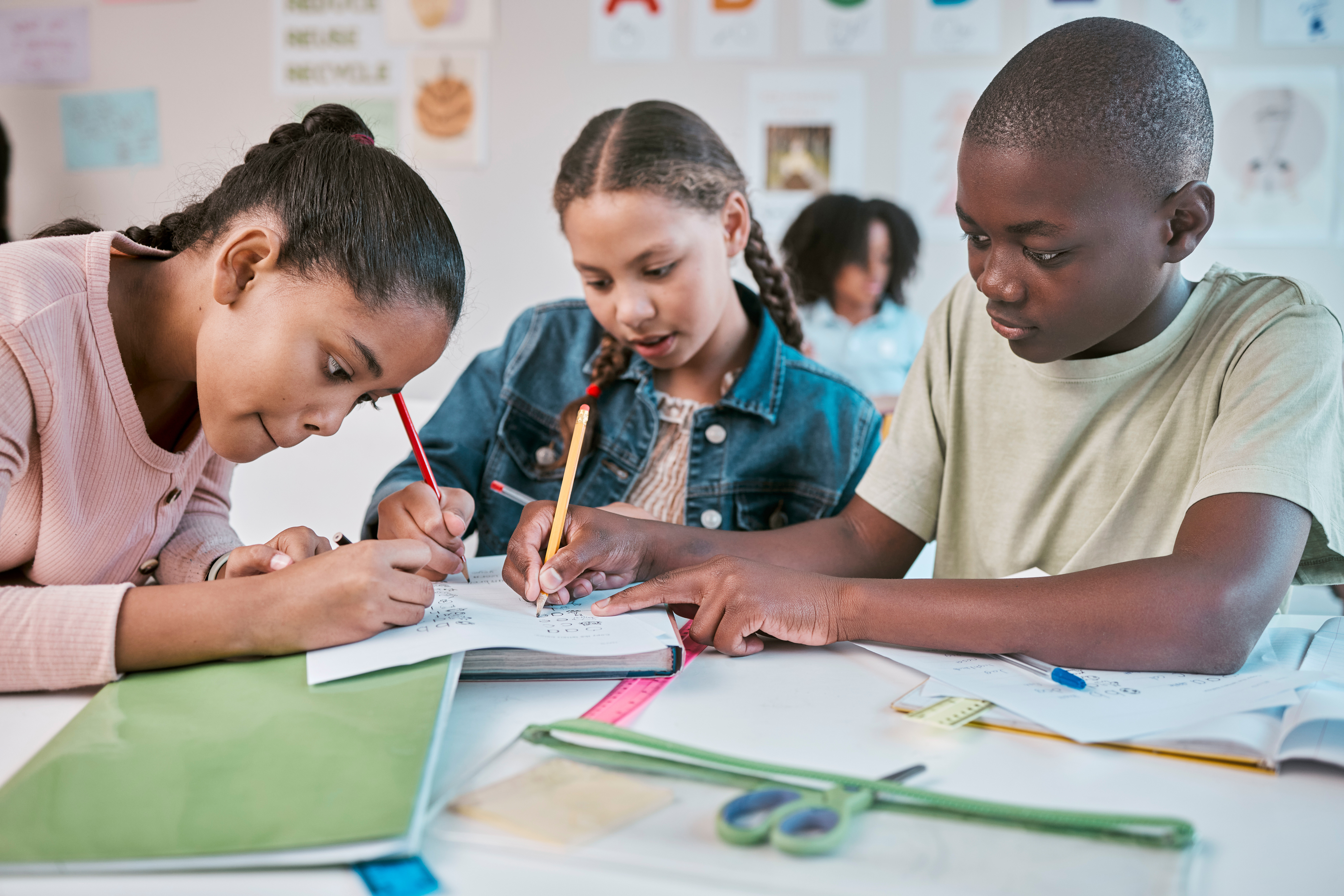 Three preteens, 2 girls and 1 boy, sit at a school desk working on a project together
