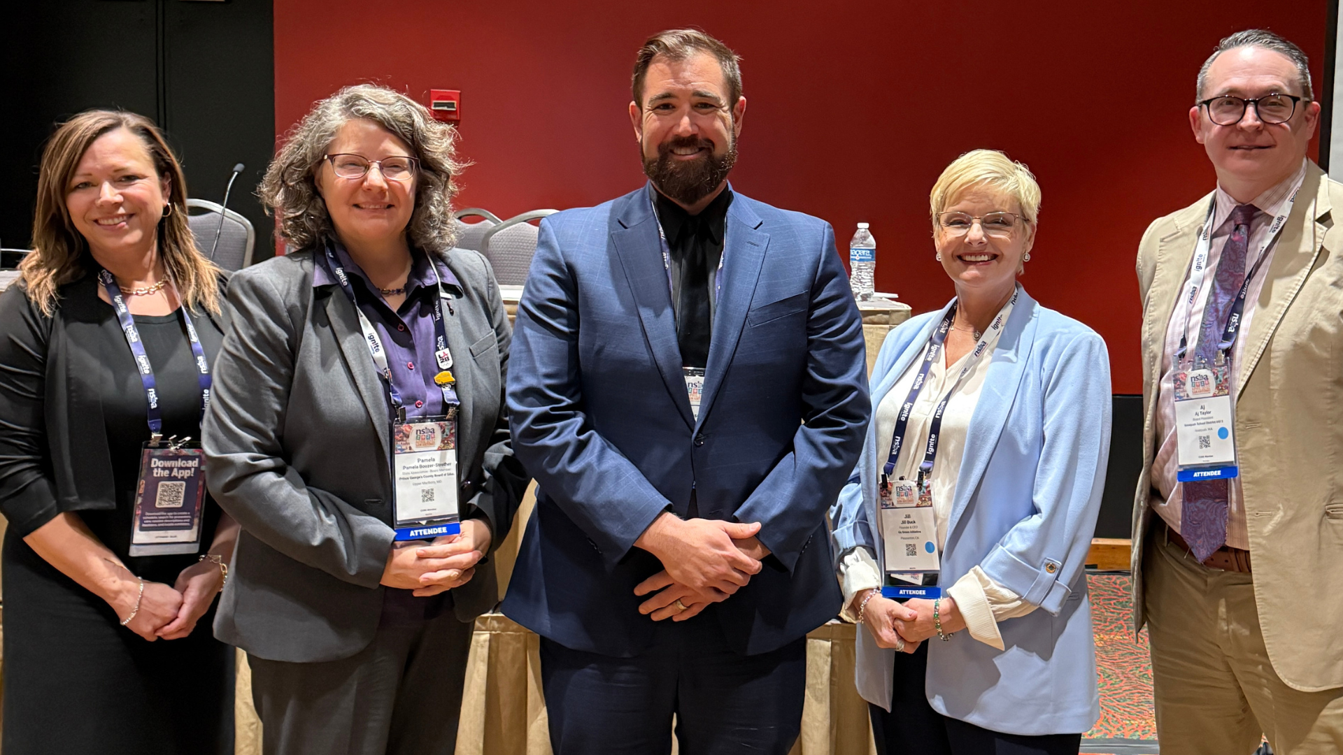 Three women and two men stand together and pose for a photo after making a presentation at a conference. 