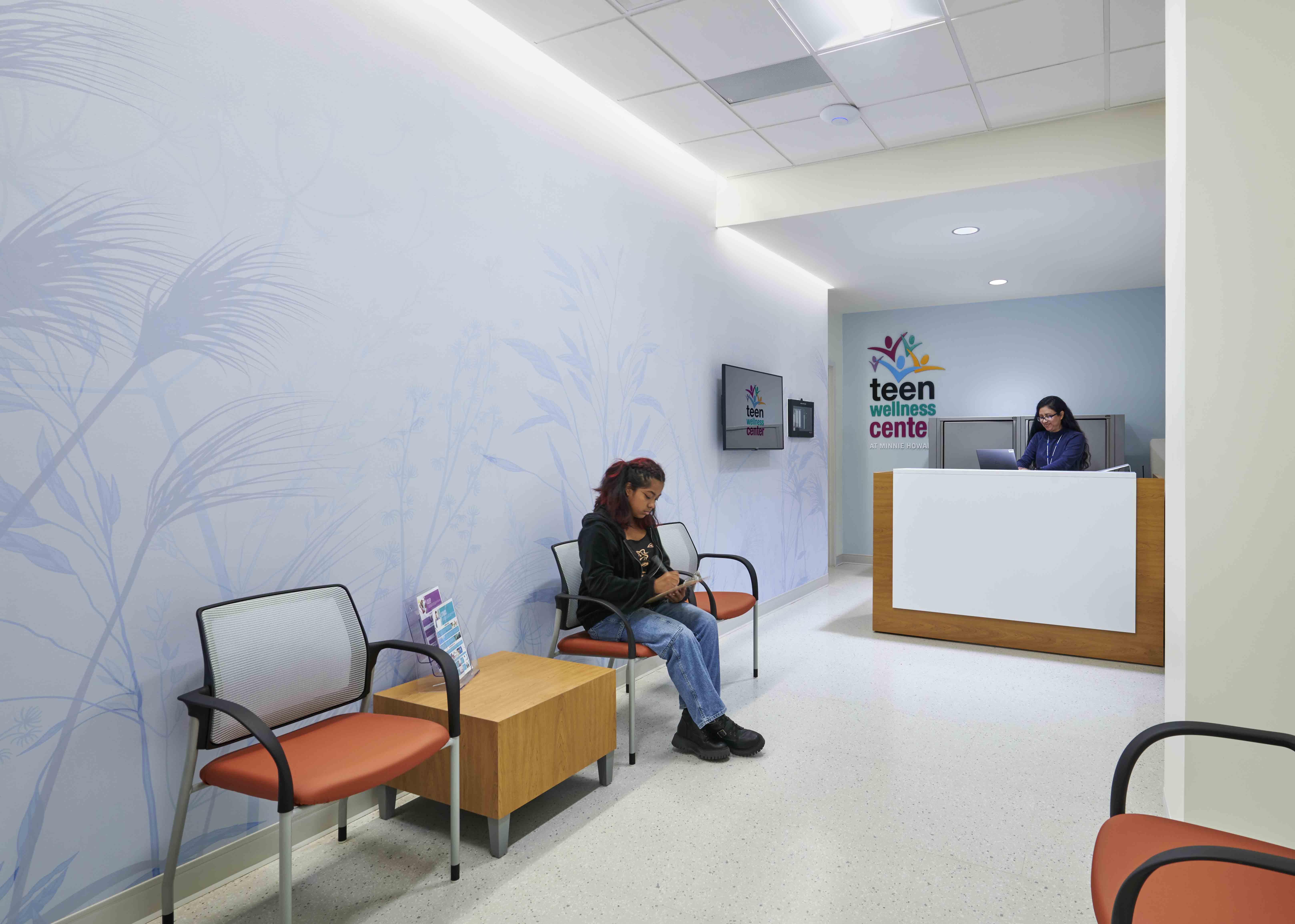 A student sits in a chair in the hallway of a bright, new school building 