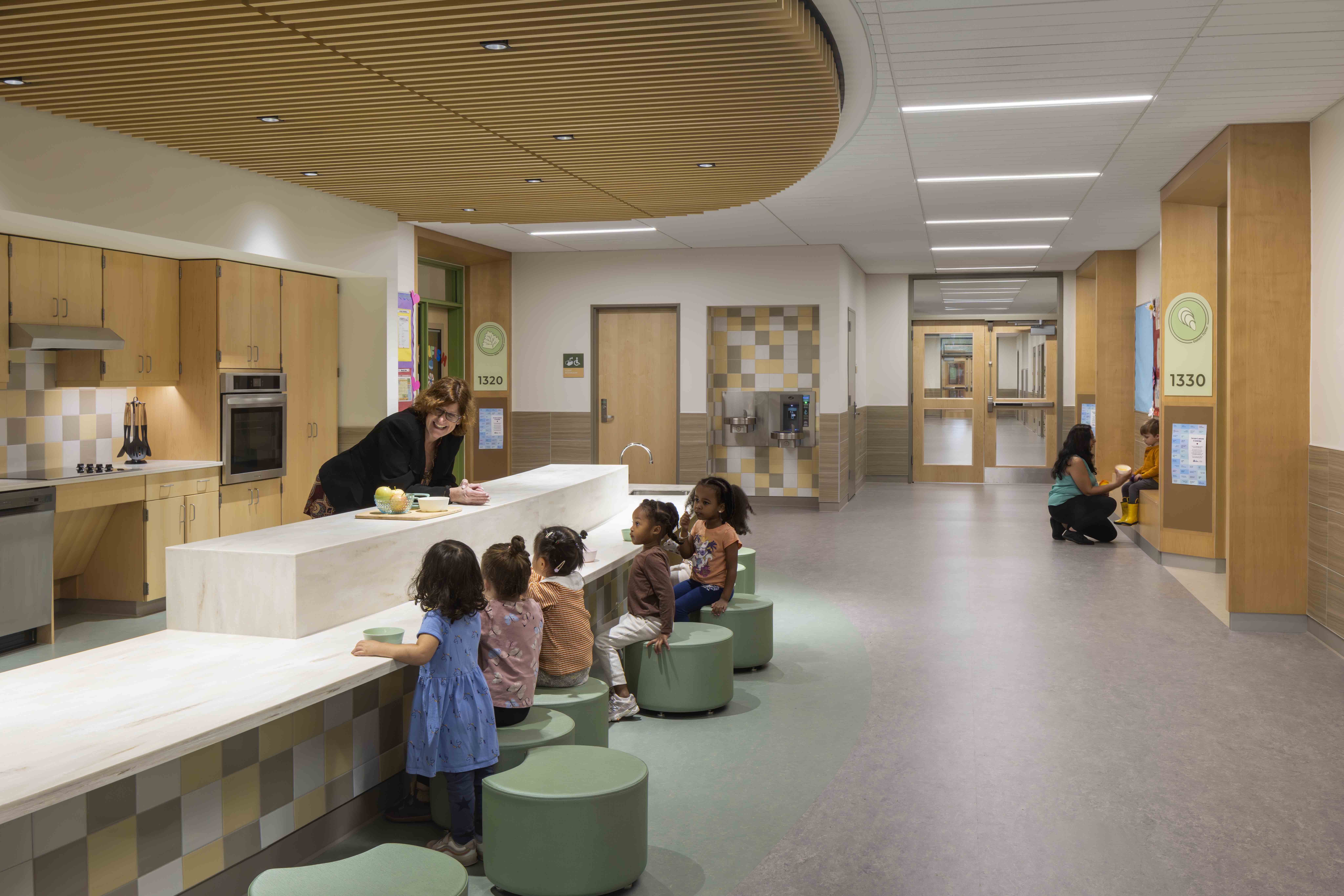 A group of preschool children sit on comfy stools and talk to a teacher.