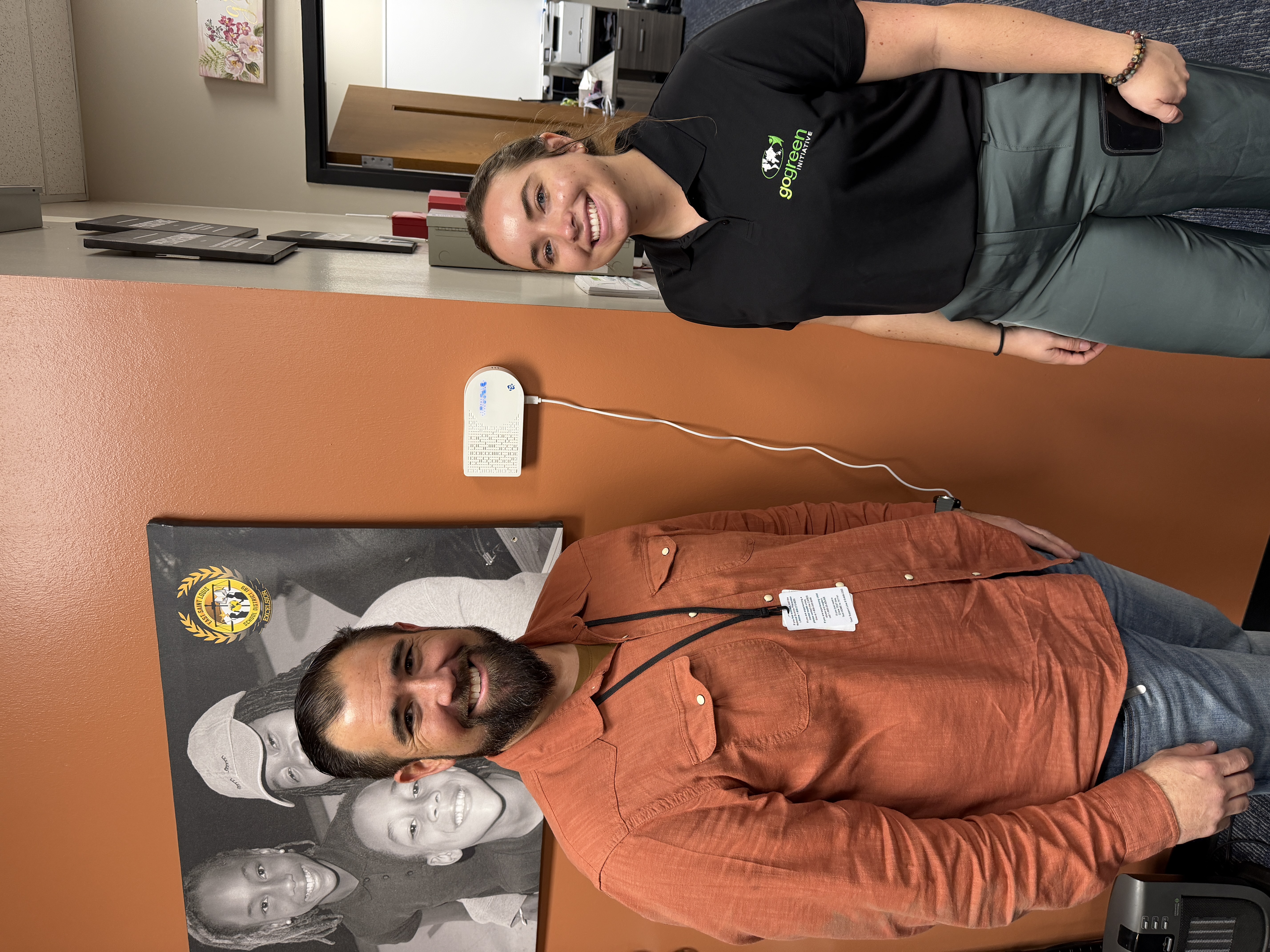 Individuals smile and stand in front of an air quality reader