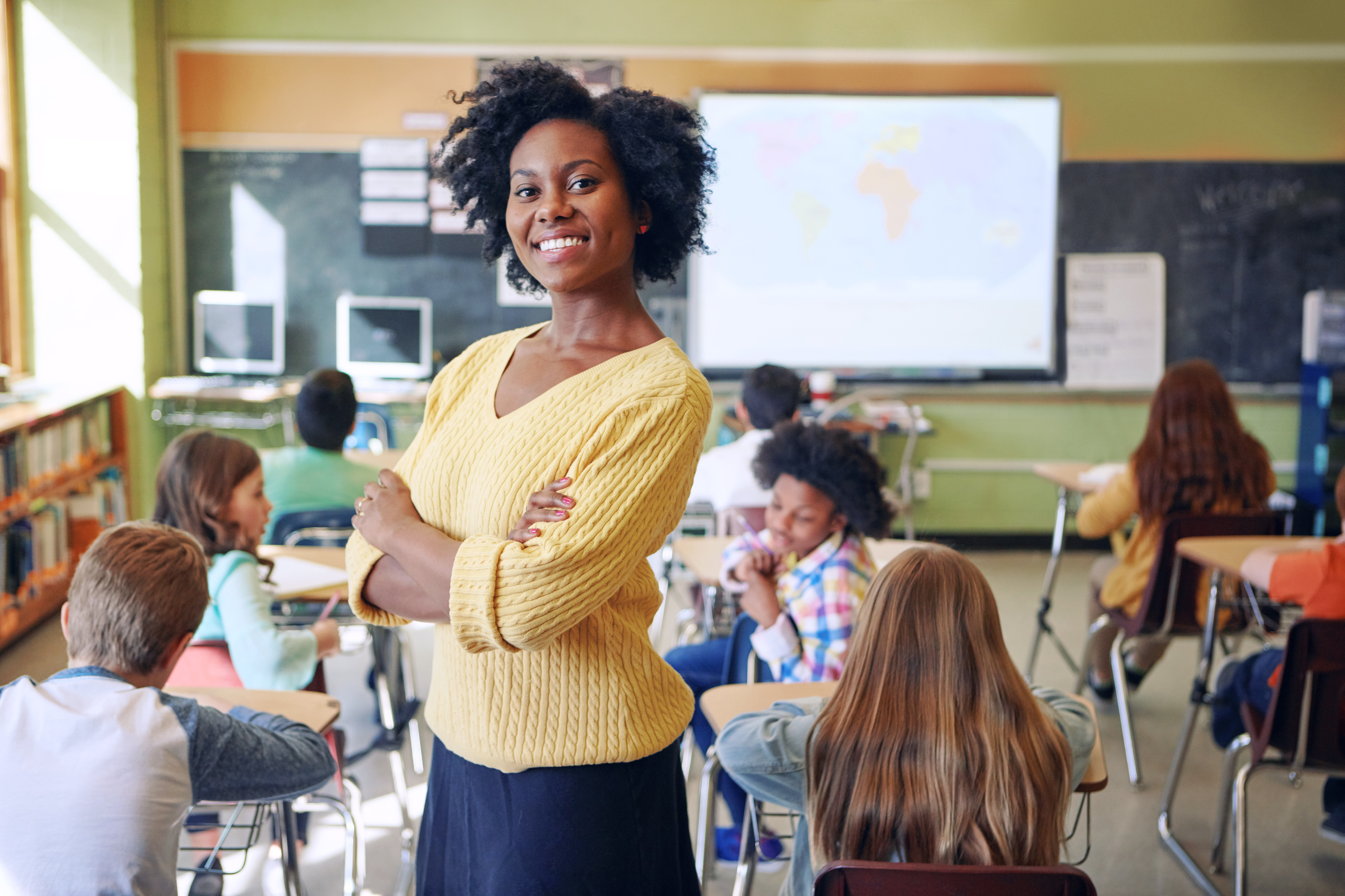 A female teacher stands in her classroom surrounded by her students.talk in a hallway