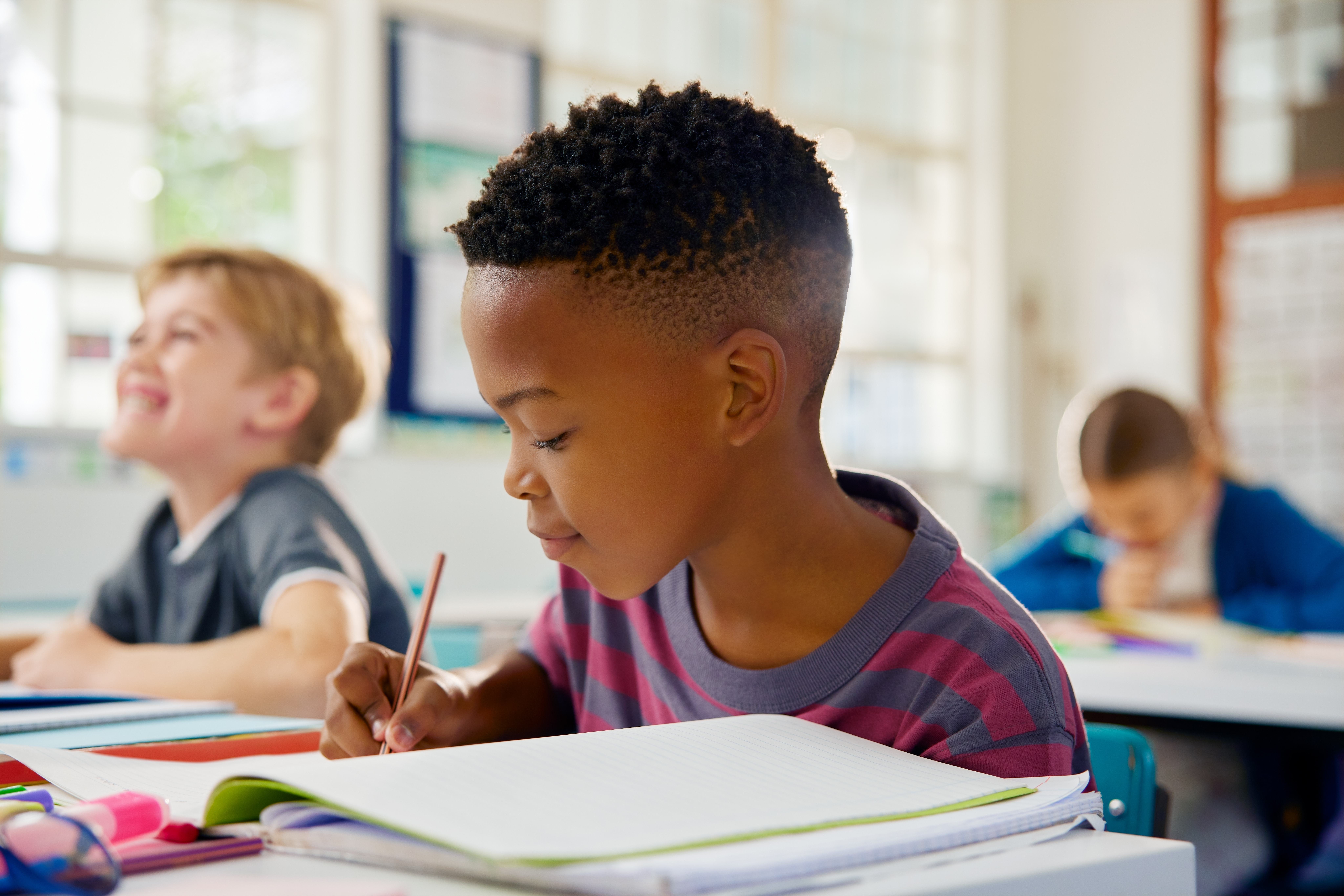 A young boy writes in a notebook during class. 