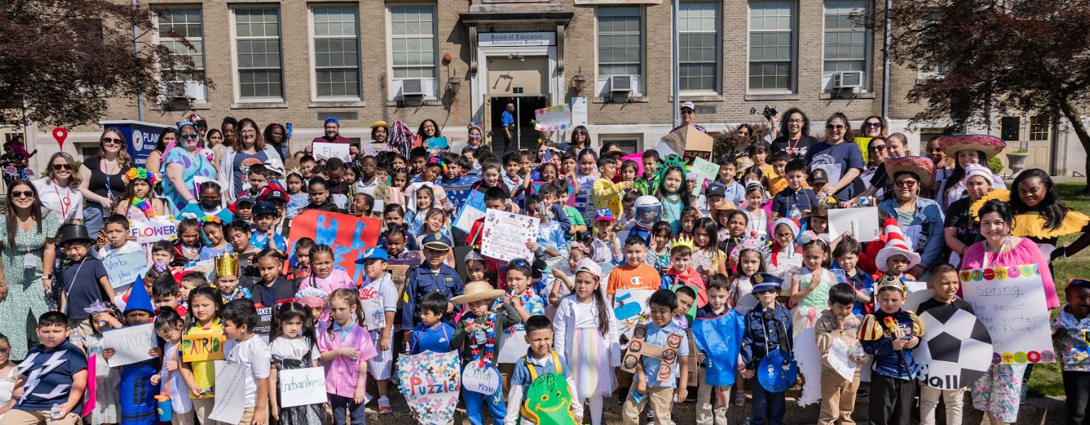 Dozens of young children parade in costume in front of their school. 