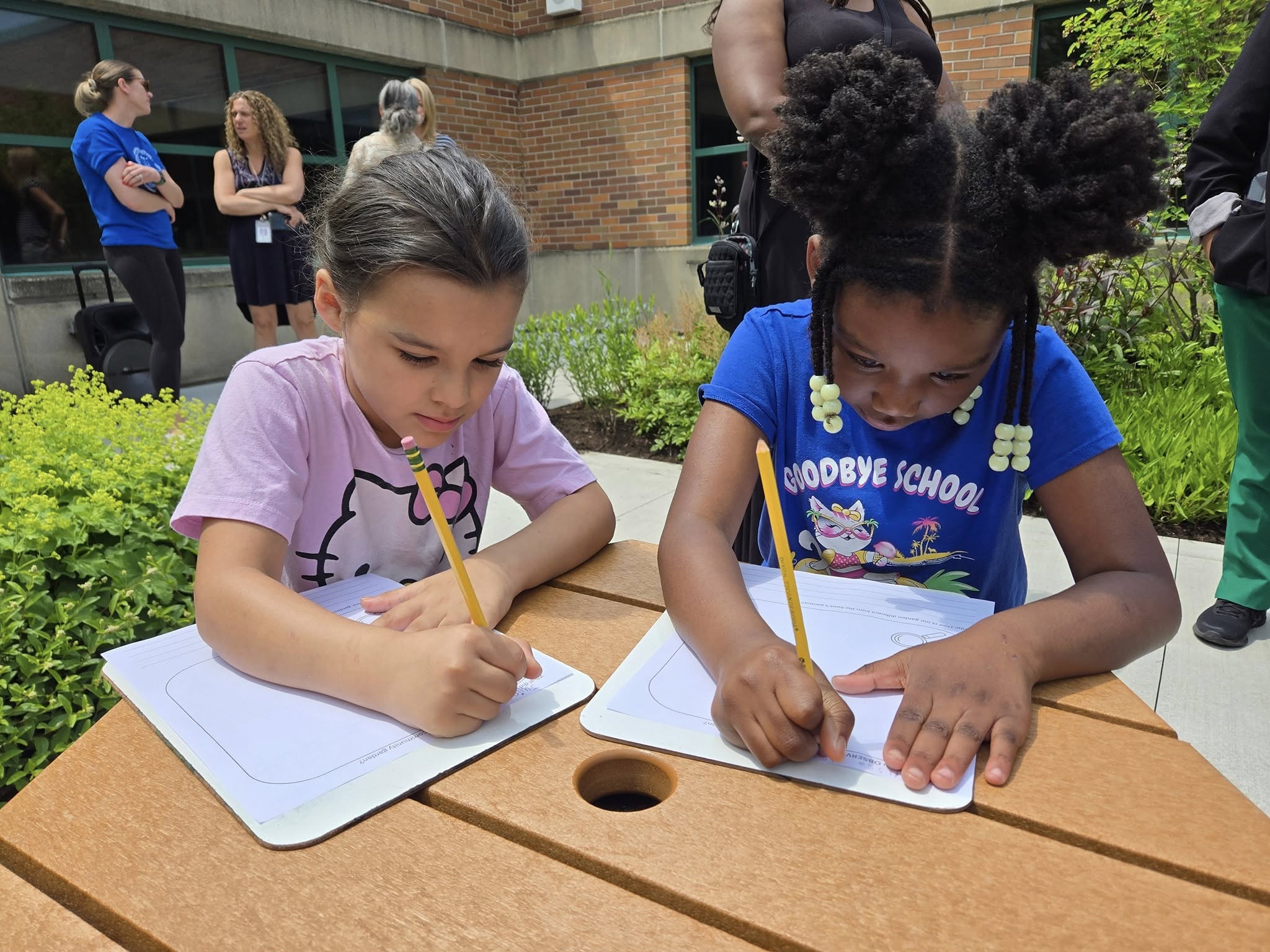 Two elementary-age girls enjoy a writing project outdoors.