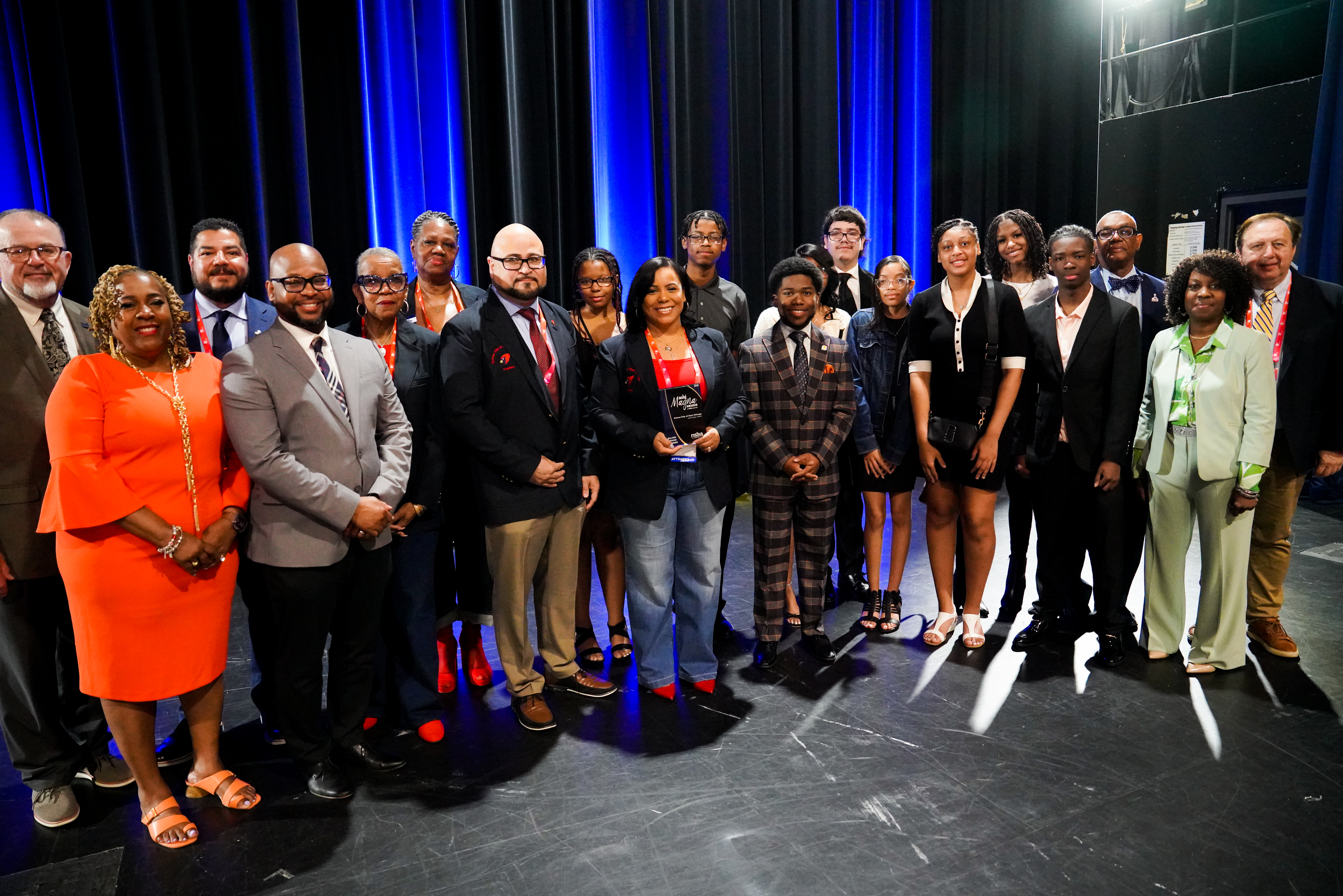 A large group of school leaders and students stand together after receiving an award plaque. 