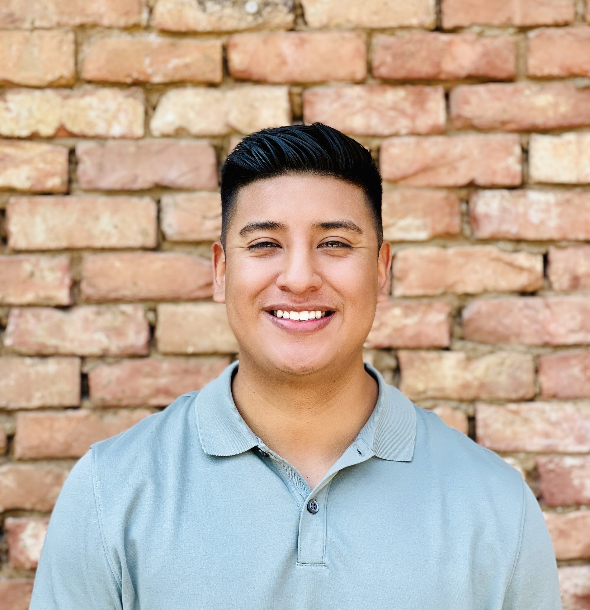 A person smiling in front of a brick wallDescription automatically generated