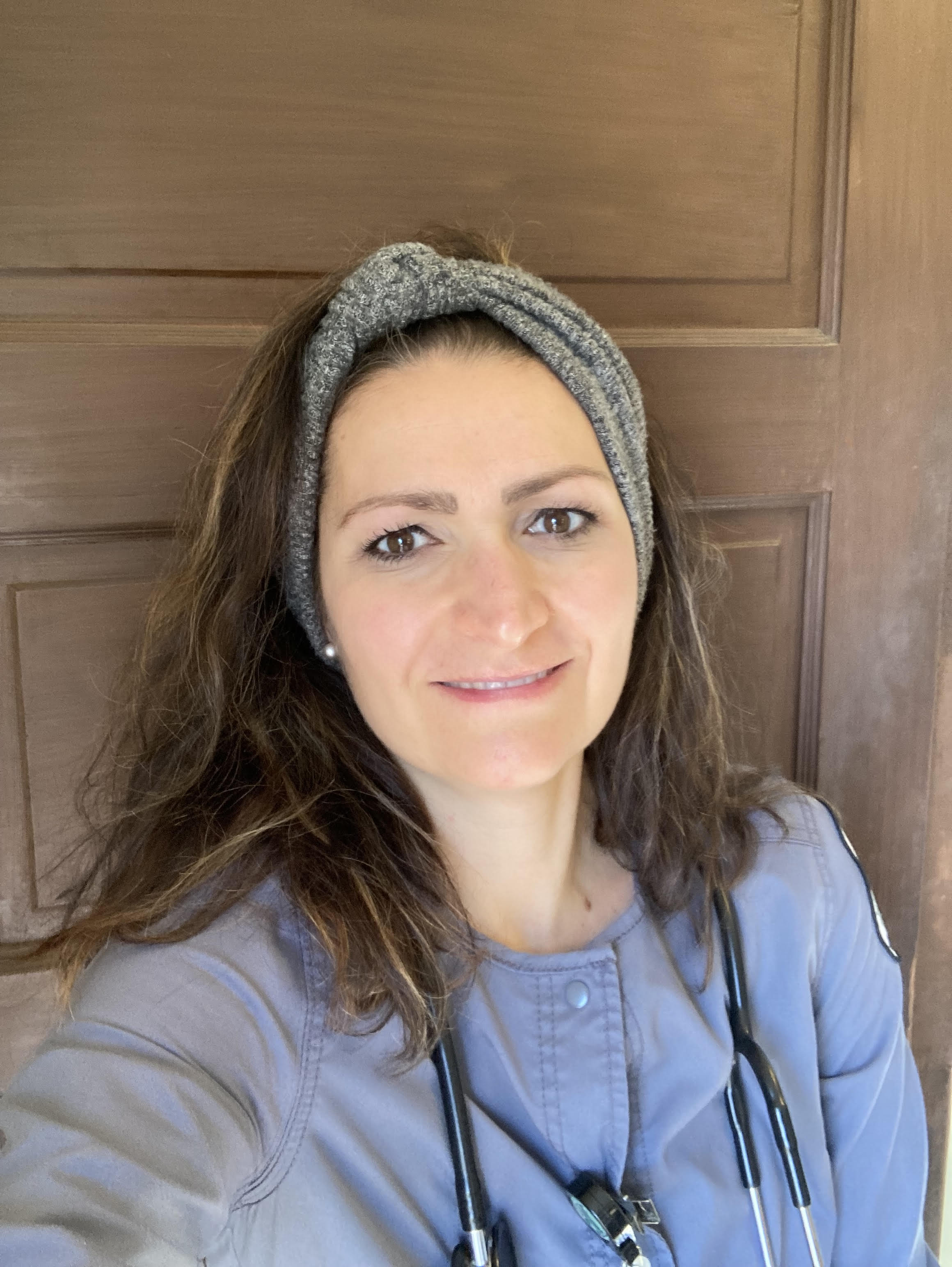 Headshot of Theresa Smith smiling at the camera. She is wearing blue nursing scrubs and standing in front of a wooden door.