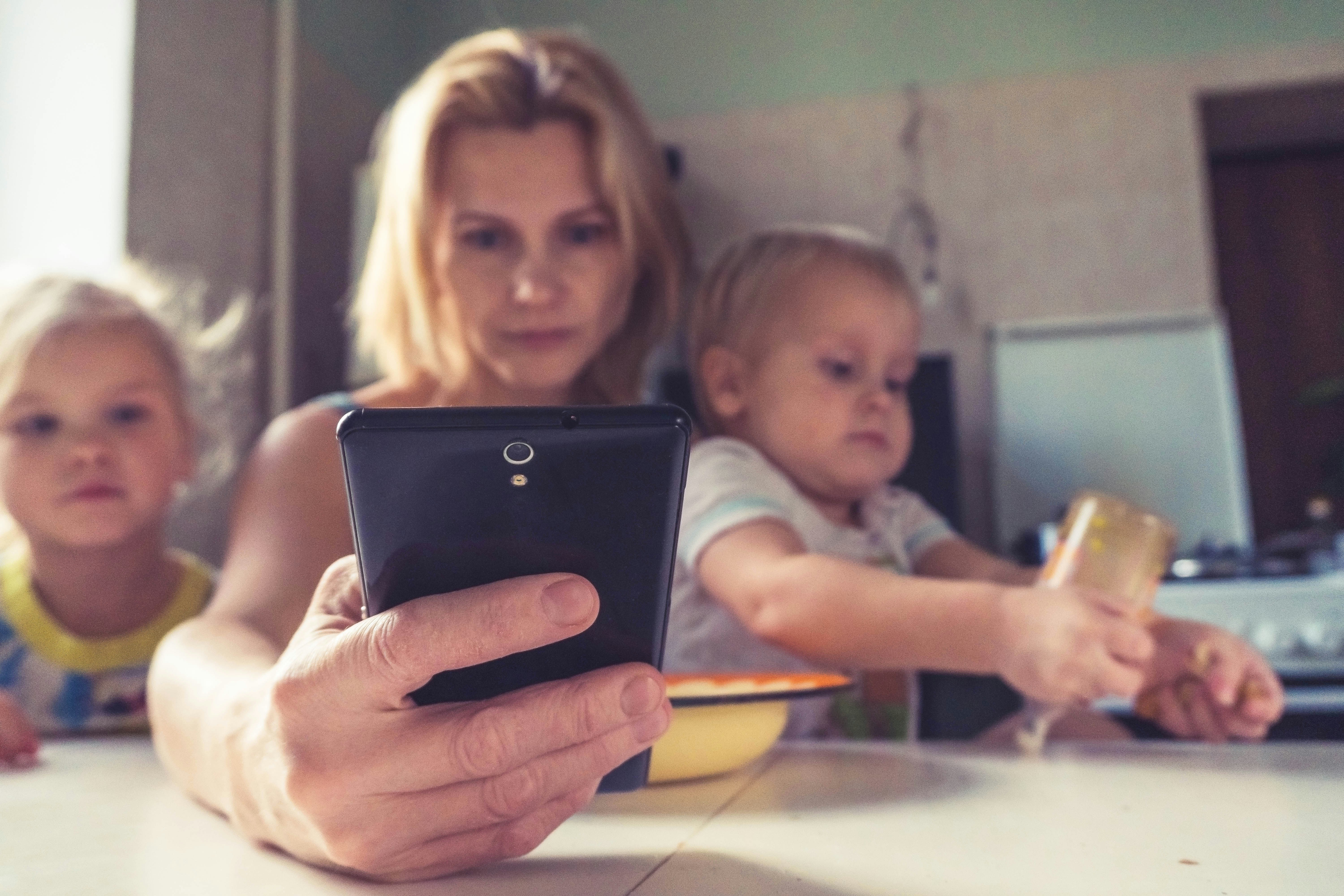 Mom working on phone with 2 kids on lap