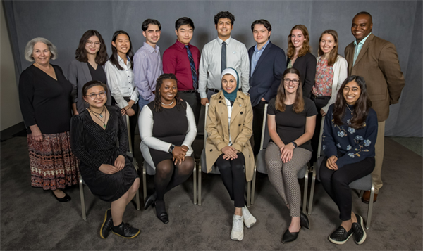 Two rows of men and woman. The backrow is standing side-by-side smiling at the camera. The front row is sitting in chairs smiling at the camera.