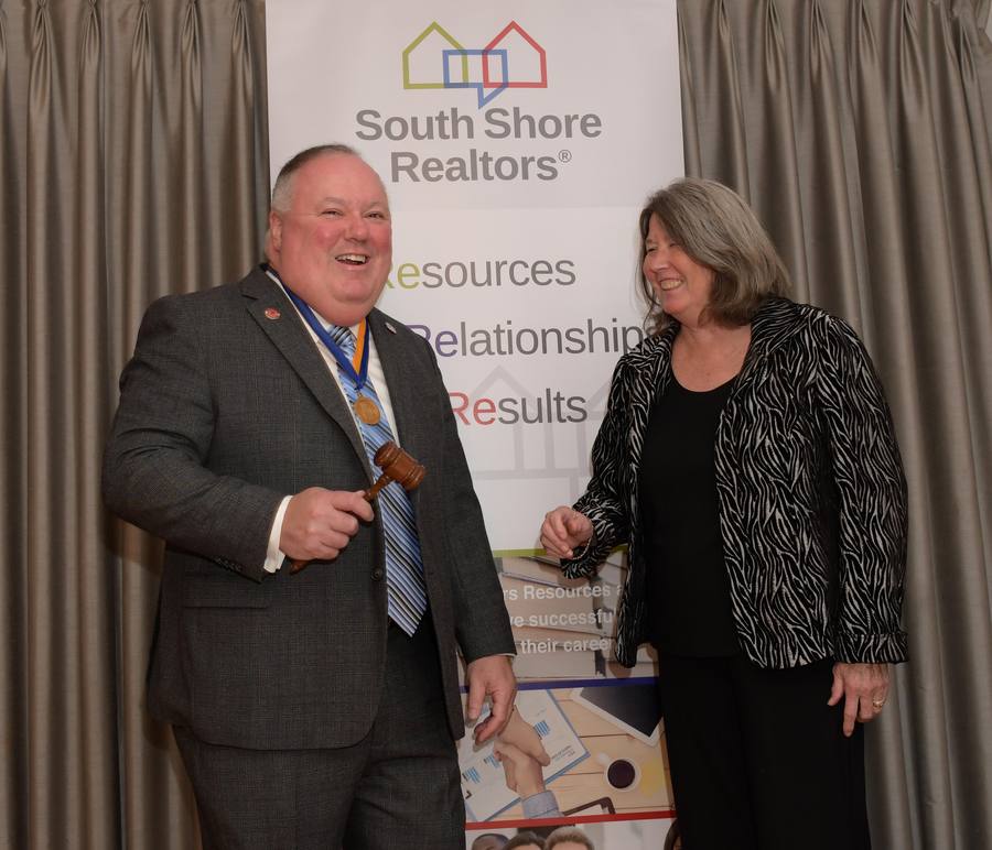 Outgoing and incoming leadership sharing the gavel in front of a South Shore Realtors banner