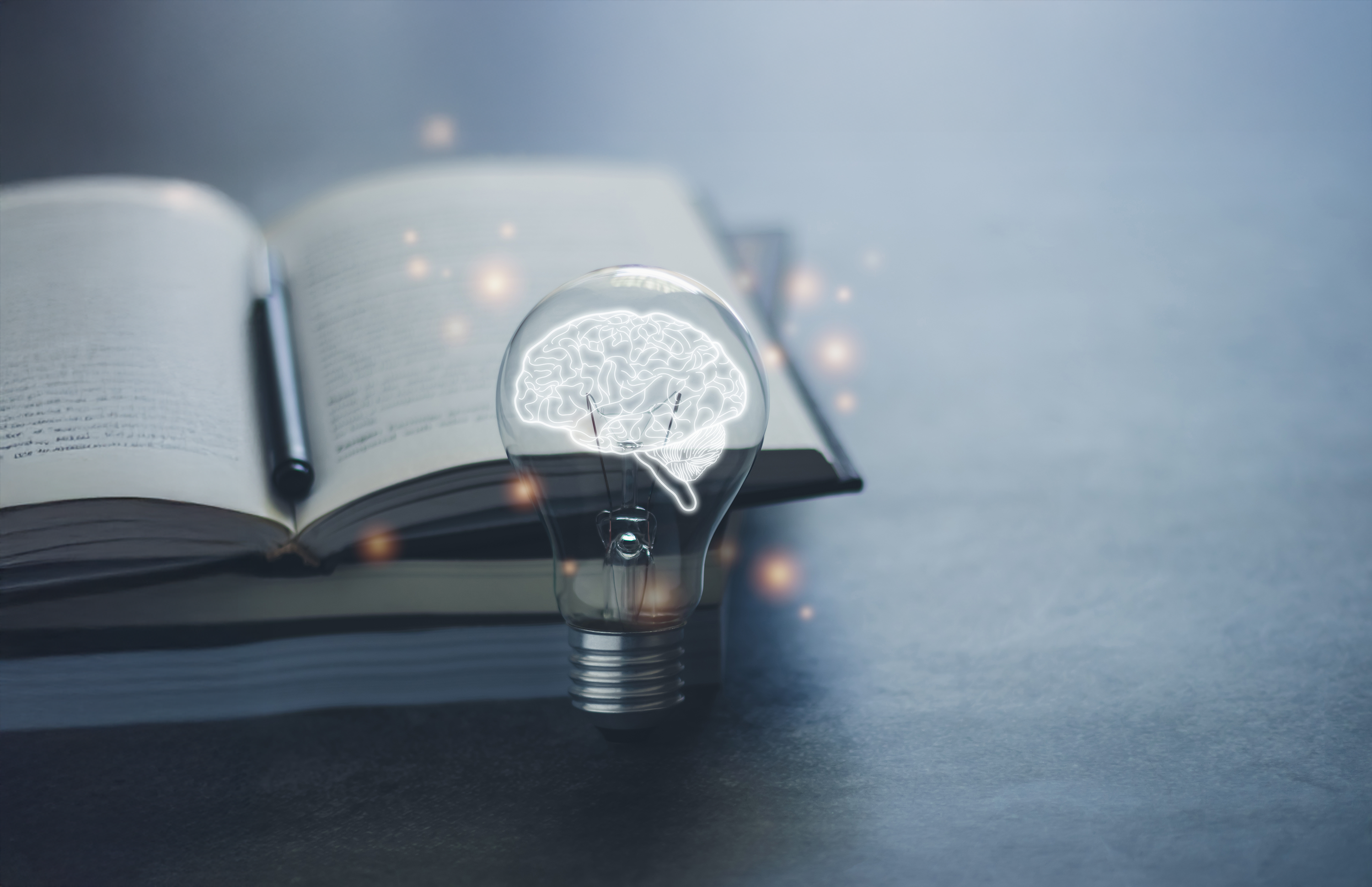Open book with pen behind a lightbulb with glowing brain