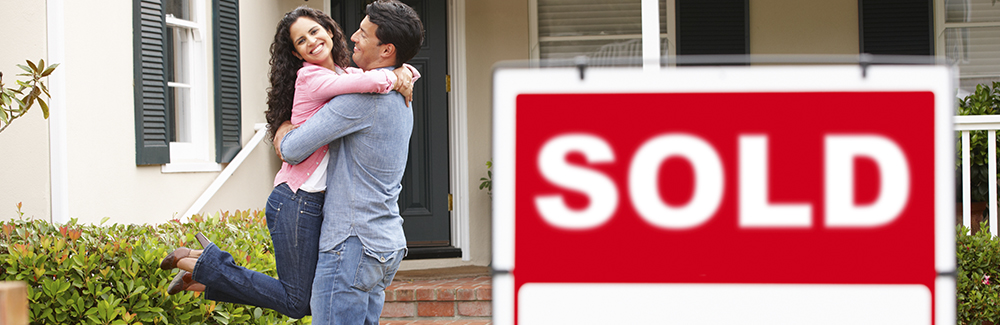 Couple outside home with sold sign Couple outside home with sold sign
