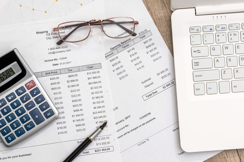 Calculator, pen, glasses, laptop and papers on desk