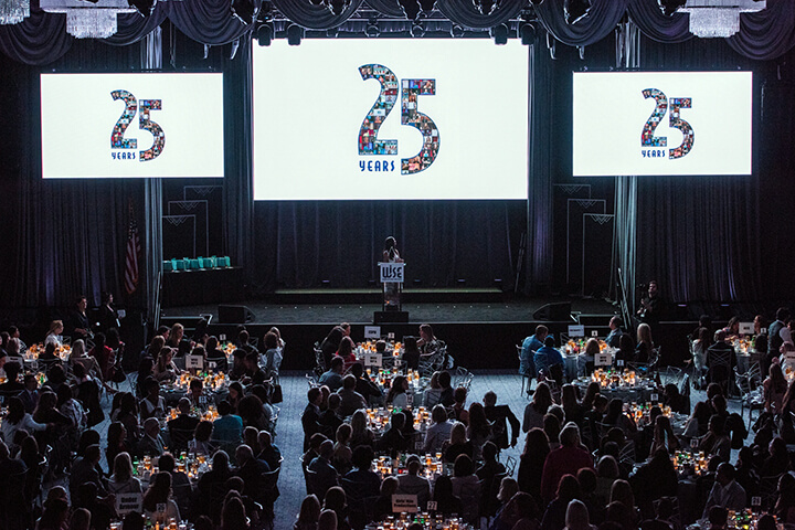 stage with 3 white screens showing 25 years and event attendees sitting around tables at the WISE WWOY 2019 Award Luncheon