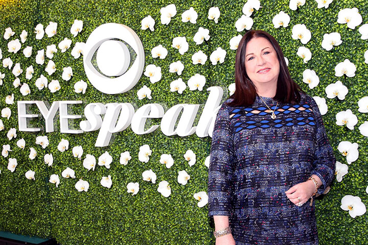 Jo Ann Ross standing in front ofa grass wall backdrop that has the 