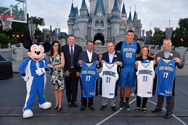 Micky Mouse, Catherine Carlson (second from left) and team at Disneyland Orlando with some team members holding Orlando Magic jerseys 