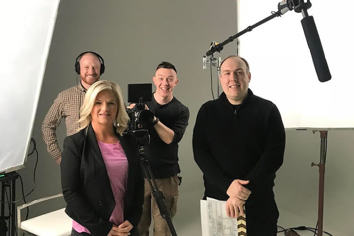 Jade Larrabee and staff at Kohl’s Photo Studio posing for a picture during a photography set with a professional camera, microphone and white backdrop stands