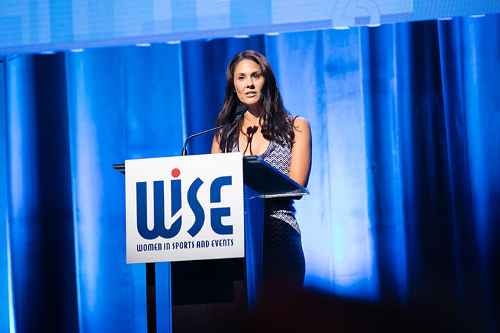 Tracy Wolfson on stage speaking as the emcee of the award luncheon