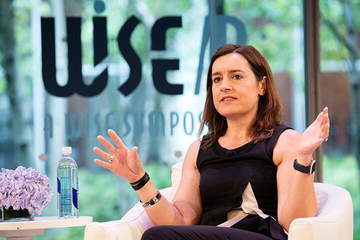 Sarah Robb O'Hagan sitting in a chair with a bottle of water beside her on a table giving a presentation