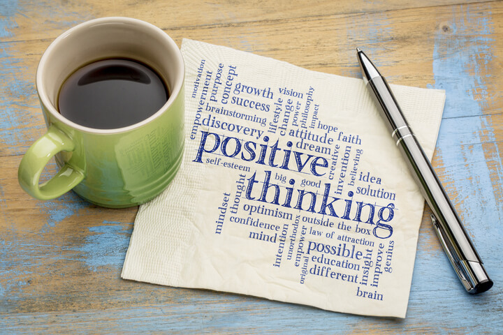 A bunch of words that refer to positive thinking written on a napkin, surrounded by a pen and a mug of coffee.