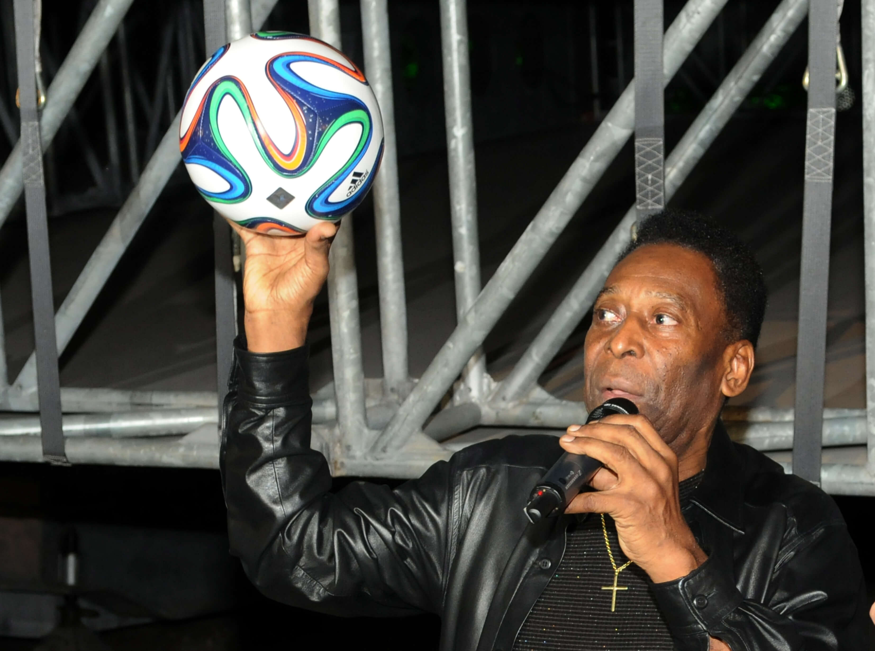 A man holding up a soccer ball whilst giving a presentation/speech